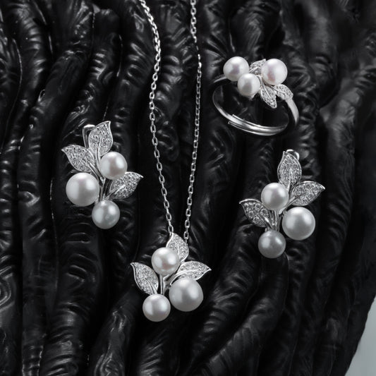 Pearl jewelry set including necklace, earrings, and ring on a textured black surface.