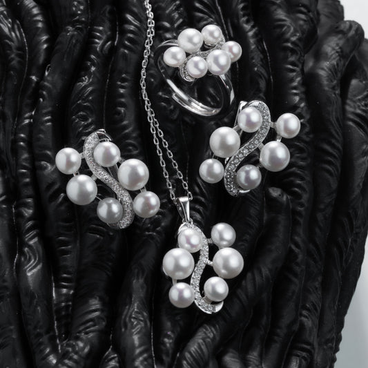 Pearl jewelry set including necklace, earrings, and ring on a dark textured surface