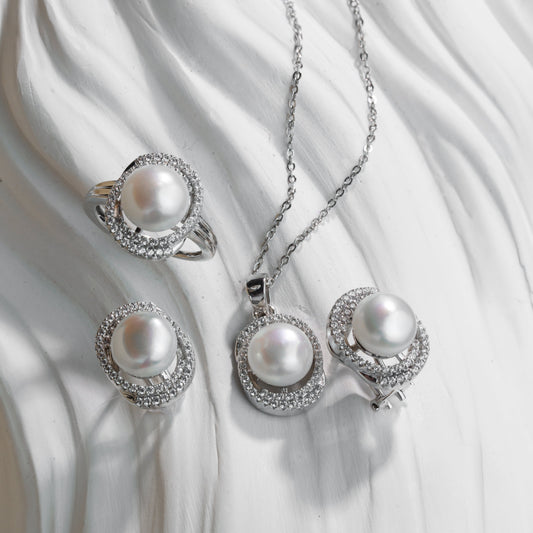 Pearl jewelry set with necklace, ring, and earrings on a white fabric background