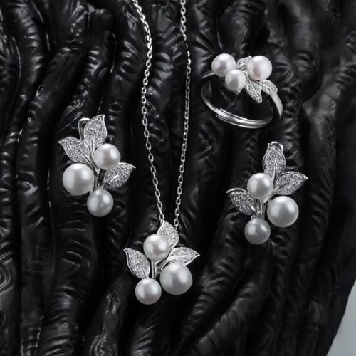 Pearl jewelry set including necklace, earrings, and ring on a textured black surface.