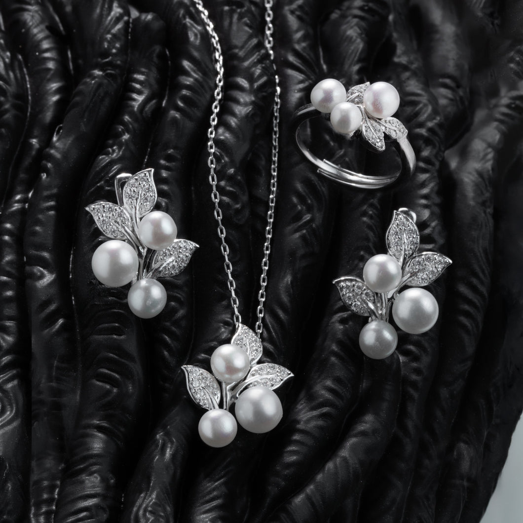 Pearl jewelry set including necklace, earrings, and ring on a textured black surface.