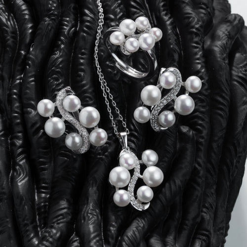 Pearl jewelry set including necklace, earrings, and ring on a dark textured surface