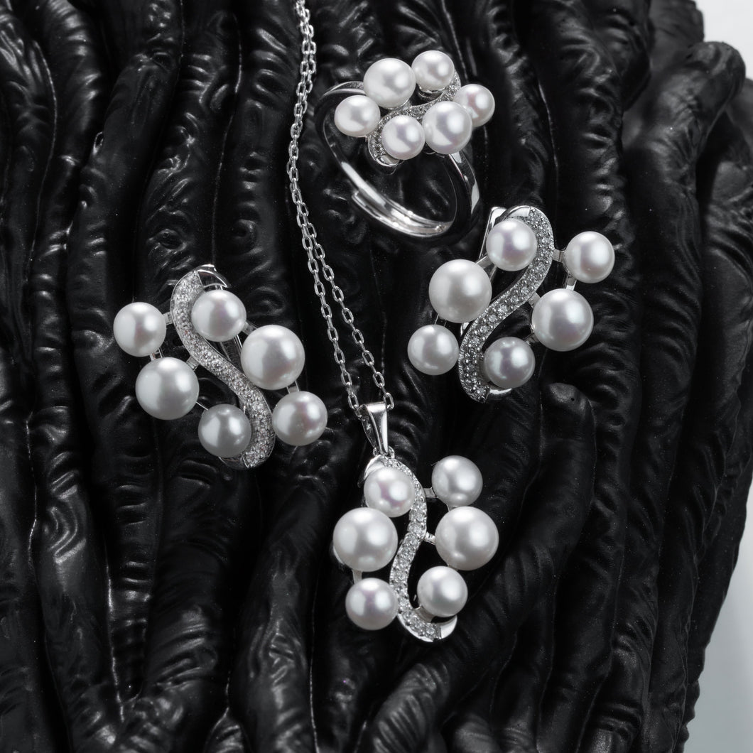 Pearl jewelry set including necklace, earrings, and ring on a dark textured surface