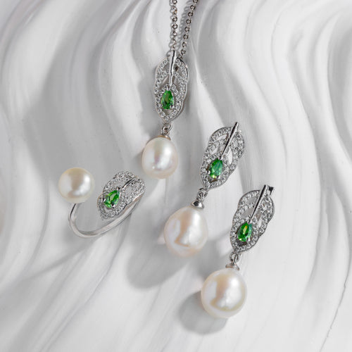Pearl jewelry set with green gemstones on a white fabric background