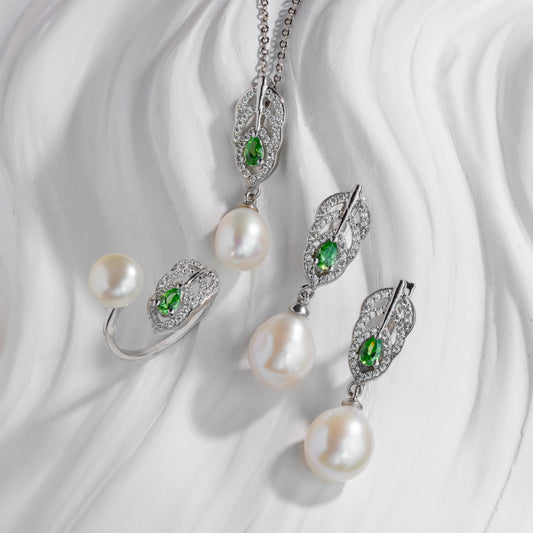Pearl jewelry set with green gemstones on a white fabric background